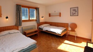 Une chambre avec deux lits, une petite table, une chaise, une fenêtre avec des rideaux et une étagère fixée au mur, sur laquelle est posée une image.