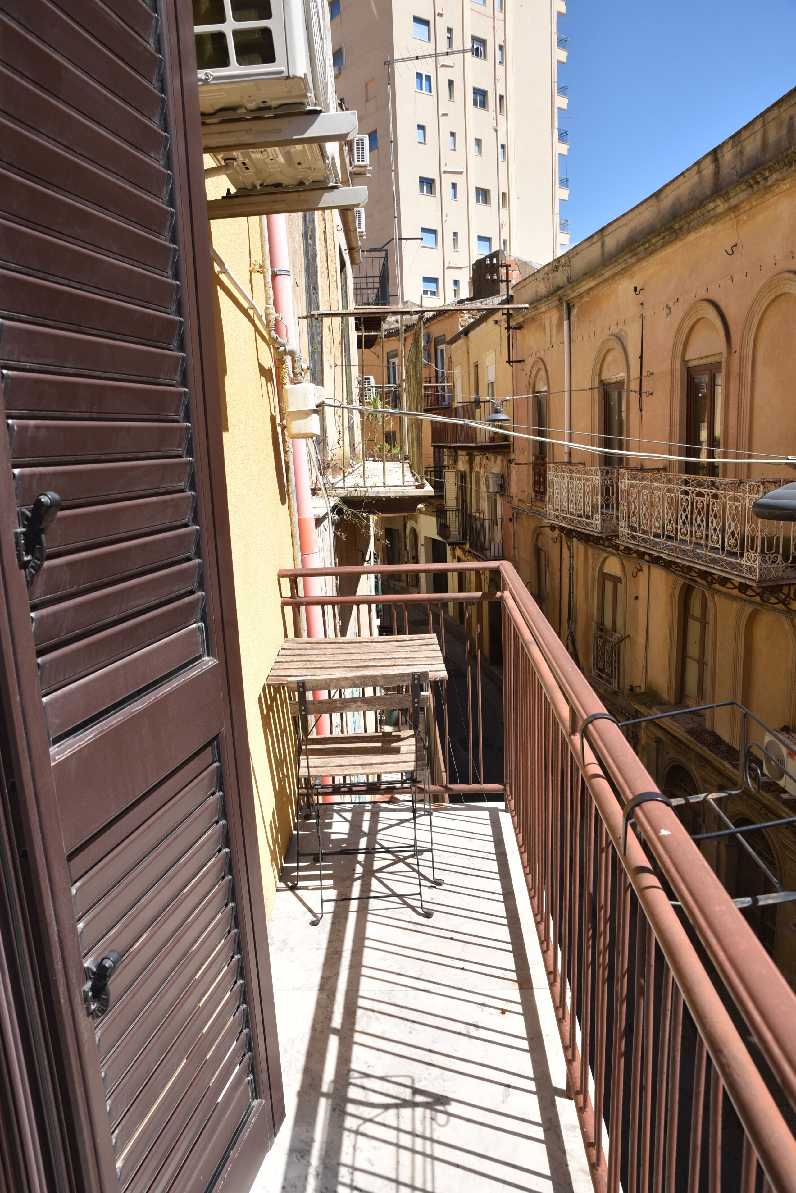 A balcony with a metal railing, a wooden table, and a view of adjacent buildings.