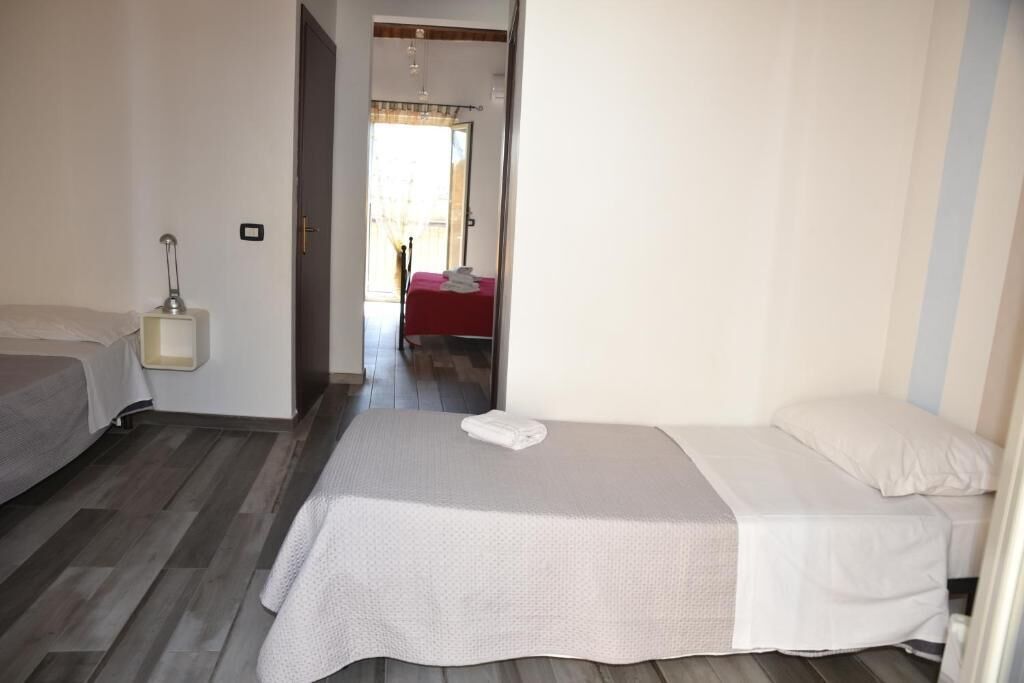 Habitación de hotel con dos camas, una mesita de noche y vista a través de una puerta abierta.