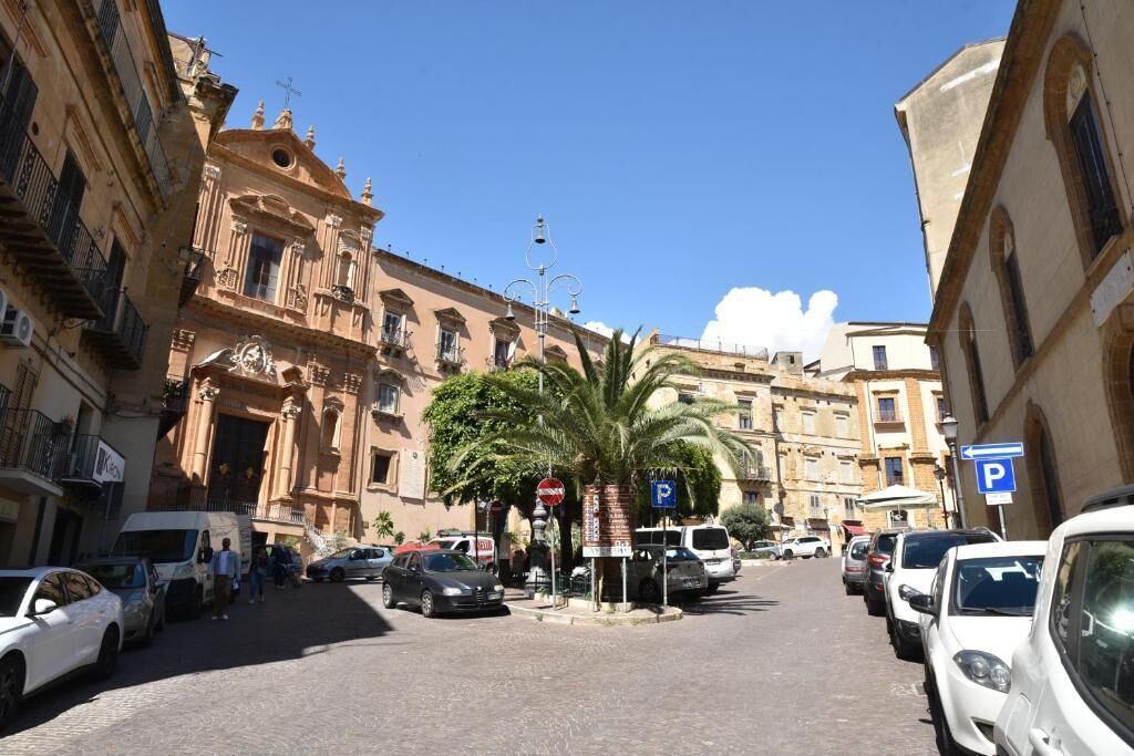 Calle con coches aparcados, una palmera y edificios históricos.