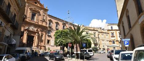 Calle con coches aparcados, una palmera y edificios históricos.