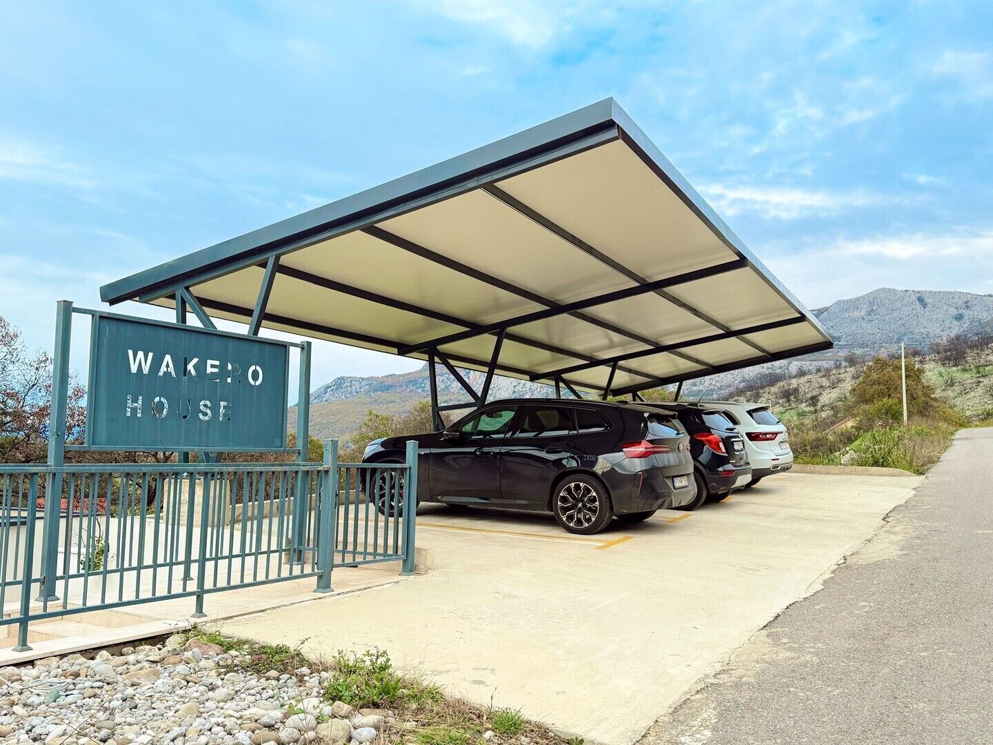 A parking area with a covered carport, a sign reading 'WAKE HOUSE,' and two parked vehicles.