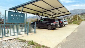 Un espace de stationnement doté d’un abri-voiture, une pancarte indiquant « WAKE HOUSE », et deux véhicules garés.