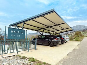 Un área de estacionamiento con una marquesina cubierta, un letrero que dice 'WAKE HOUSE' y dos vehículos estacionados.