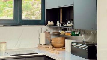 A modern kitchen with dark cabinetry, a marble countertop, and a window with a view of greenery.