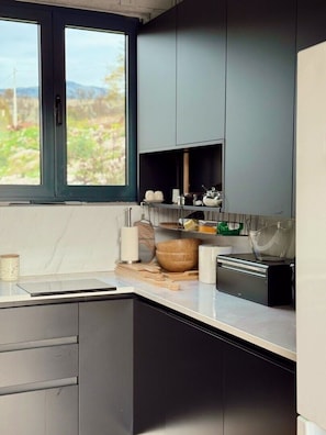 Cocina moderna con armarios oscuros, encimera de mármol y ventana con vistas a zonas verdes.