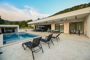 A modern outdoor pool area with a table and chairs, a ping pong table, and a covered seating area.