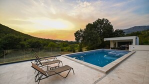 Une piscine sur le toit, dotée de chaises longues, d’une balustrade en verre et offrant une vue sur le paysage.