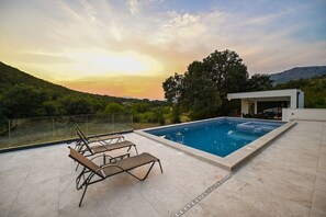 Una piscina en la azotea con sillones de descanso, barandilla de cristal y vistas al paisaje.