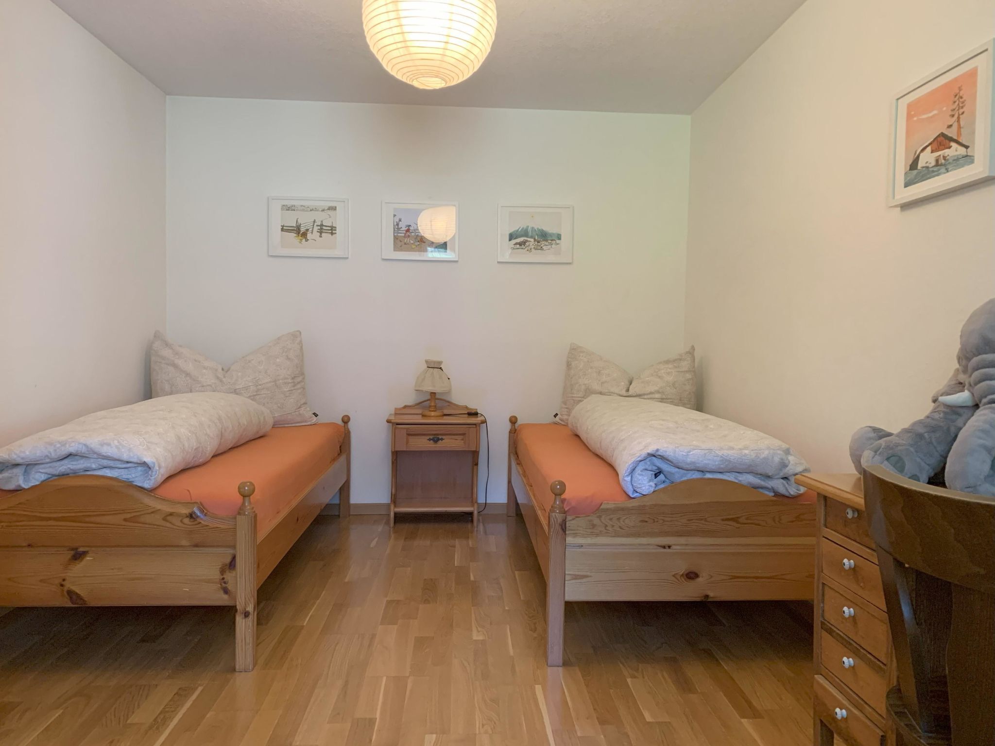 A room with two wooden beds, a nightstand, a lamp, and three framed pictures on the wall.