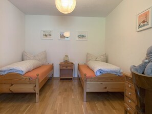 Ein Zimmer mit zwei Holzbett, einem Nachttisch, einer Lampe und drei gerahmten Bildern an der Wand.