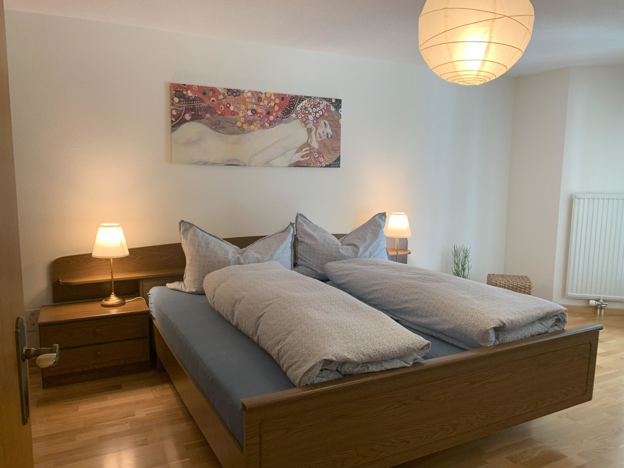 Une chambre à coucher avec un lit en bois, deux lampes de chevet, un tableau au mur et un radiateur.