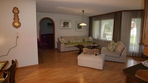 A living room with a sofa, ottoman, and a dog. There is a wooden floor, a lamp, and a window with curtains. - Cadras 10 Appartement/Fewo, Bad, WC, 2 Schlafräume 3 Zimmerwohnung - 4 Betten by Interhome (Tinizong)