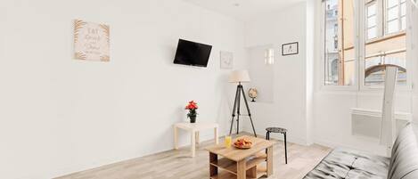 A modern living room with a sofa, a small table with a flower vase, a lamp, and a TV on the wall.