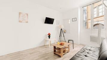 Una sala de estar moderna con un sofá, una mesita de madera con un jarrón de flores, un trípode y un televisor de pantalla plana montado en la pared.