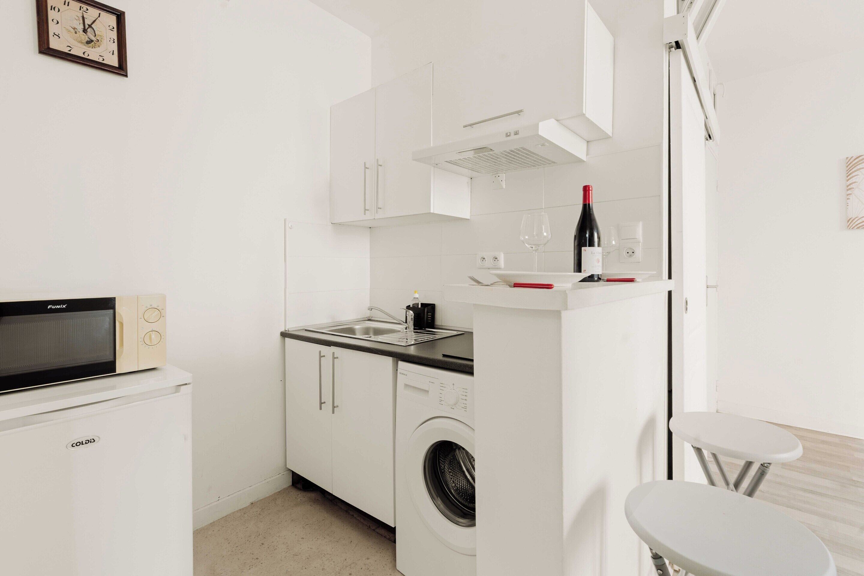 Een kleine keuken met een magnetron, oven, spoelbak en een wijnfles op het aanrecht.