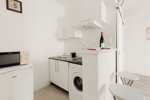 Uma kitchenette compacta com micro-ondas, forno, pia e uma garrafa de vinho na bancada.