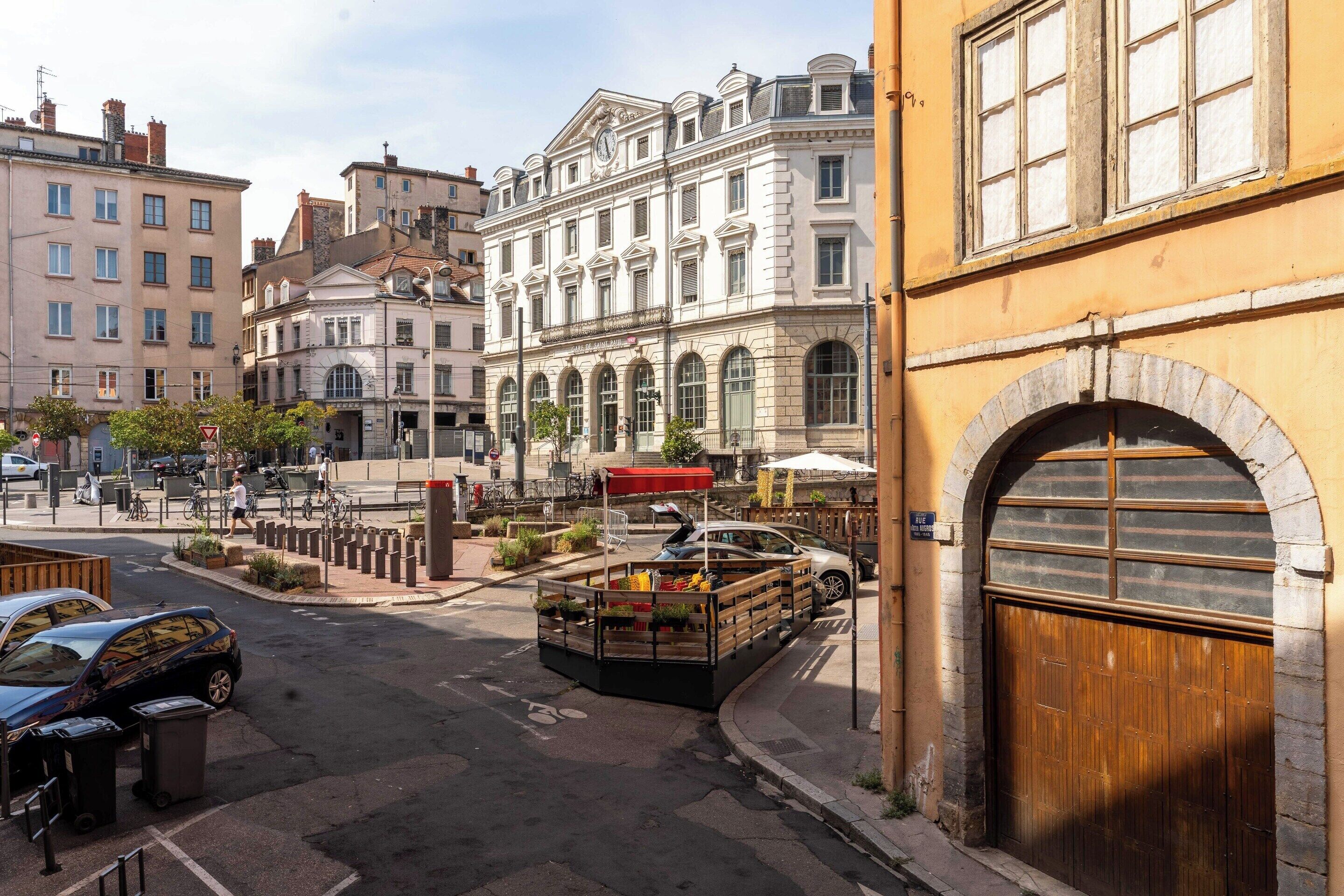 Une vue de rue avec un bâtiment portant l’inscription « Gare de Saint-Paul » et un véhicule stationné doté d’une structure en bois.