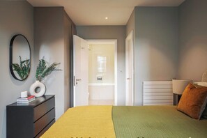 A bedroom with a bed, a dresser, a mirror, and a door leading to a bathroom. - Student Only Clay Wembley (Wembley)