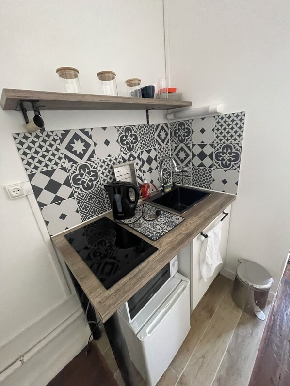 Cocina compacta con cocina por inducción negra, refrigerador blanco y azulejos de despensa con diseño.