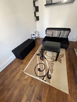 Ein Wohnzimmer mit einer schwarzen Couch, einem schwarzen Hocker und einem gemusterten Teppich.