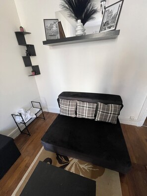 Una sala de estar con un sofá negro, un tapete estampado y estanterías negras sobre una pared blanca.