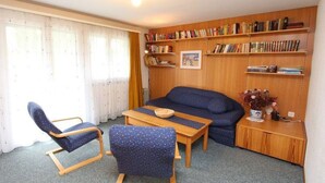 Un salon chaleureux avec un canapé, deux fauteuils, une table basse et une bibliothèque remplie de livres.