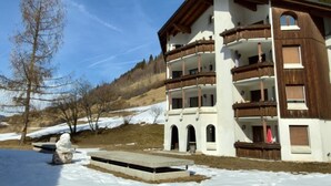 A multi-story building with balconies, a stone staircase, and a snow-covered ground. - Cadras 14 Appartement/Fewo, Dusche oder Bad, WC, 2 Schlafräume by Interhome (Savognin)