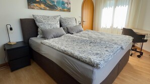 A modern bedroom with a large bed, a nightstand, a desk, and a window with curtains. - Cadras 14 Appartement/Fewo, Dusche oder Bad, WC, 2 Schlafräume by Interhome (Savognin)