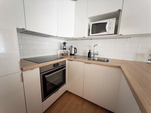 A compact kitchen with white cabinets, a stainless steel sink, a microwave, a kettle, and a built-in oven. - Cadras 14 Appartement/Fewo, Dusche oder Bad, WC, 2 Schlafräume by Interhome (Savognin)