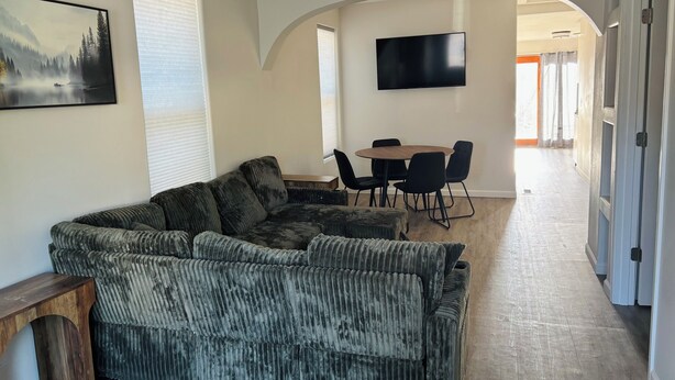 Un salon comprenant un canapé d’angle, un téléviseur à écran plat fixé au mur et un coin repas avec une table et des chaises.