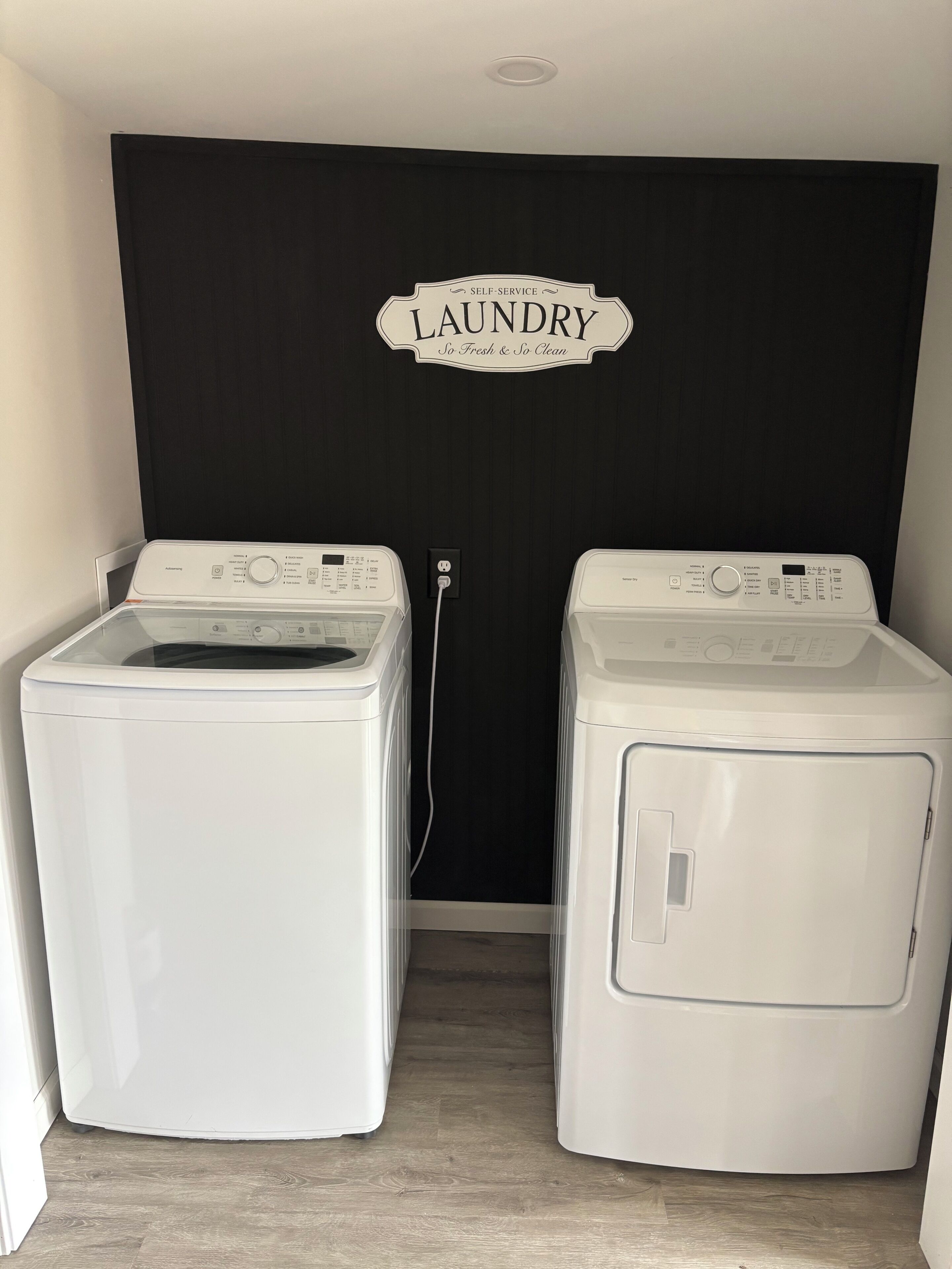Une buanderie équipée de deux machines à laver à chargement frontal, avec une pancarte au-dessus de la porte indiquant « BUANDERIE ».