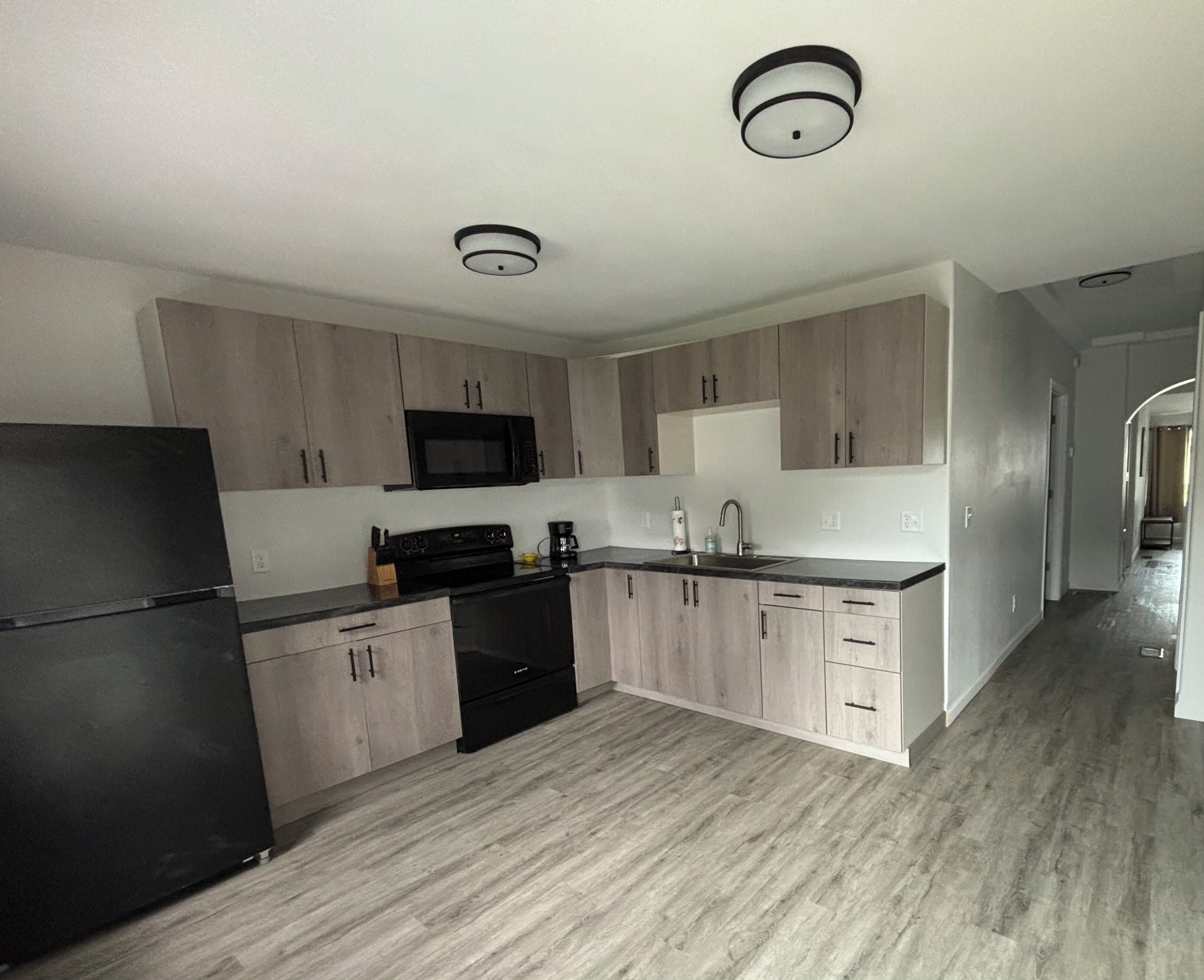 Una cocina moderna con armarios de madera clara, un refrigerador negro y un microondas.