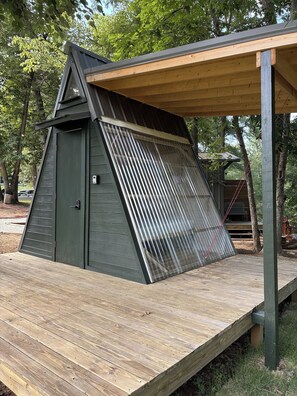 A wooden deck with a metal-framed structure, possibly a gazebo or shelter, in a wooded area.