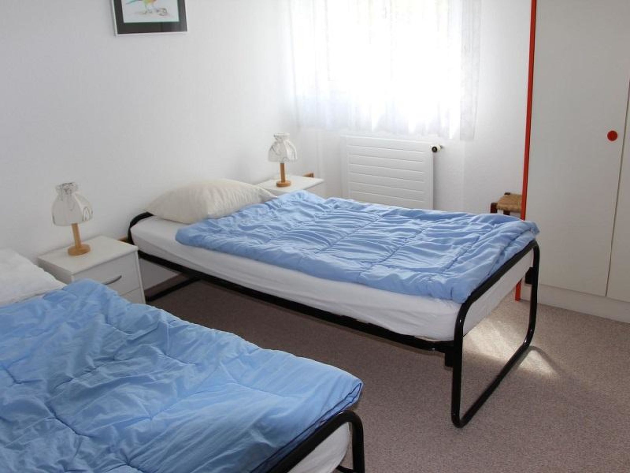A simple bedroom with two single beds, a nightstand, a lamp, and a radiator.