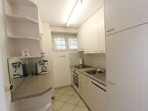 A compact kitchen with white cabinets, a built-in oven, a sink, and a window with blinds. - Las Vals B11 Appartement/Fewo, Bad, WC, 3 Schlafräume by Interhome (Savognin)