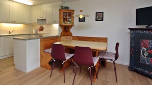 Eine kompakte Küche mit einer zentralen Kochinsel, einem Esstisch mit vier Stühlen und einem Fernseher auf einem Schrank.