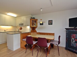 Eine kompakte Küche mit einer zentralen Kochinsel, einem Esstisch mit vier Stühlen und einem Fernseher auf einem Schrank.