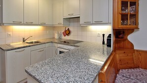 Eine Küche mit weißen Schränken, einer Granitarbeitsplatte, einem eingebauten Backofen und einem Holzschrank mit Glastüren.