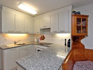 Eine Küche mit weißen Schränken, einer Granitarbeitsplatte, einem eingebauten Backofen und einem Holzschrank mit Glastüren.