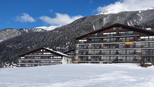 Ein mehrstöckiges Hotel mit Balkonen vor einer verschneiten Bergkulisse.