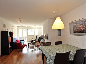 A dining area with a table and chairs, a red chair, a bookshelf, and a painting on the wall. - Las Vals E03 Appartement/Fewo, Dusche, WC, 2 Schlafräume by Interhome (Savognin)