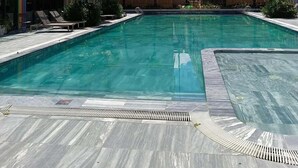 Ein Schwimmbecken mit Fliesen umgeben, umgeben von Gebäuden mit großen Fenstern und blauem Himmel.