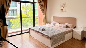 Ein Schlafzimmer mit großem Fenster, einem Bett mit gemusterten Bettwaren, einem Nachttisch und einem Wandbild.