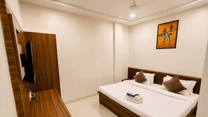 Hotelkamer met een houten garderobe, een bed met witte lakens, een plafondventilator en een kunstwerk aan de muur.