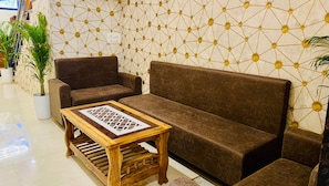 Un área de descanso moderna con un sofá marrón, una mesa de centro de madera y una pared con estampado geométrico.