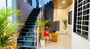 A modern interior with a staircase, potted plants, and a wooden bench. - Maa Kripa Hotel (Ujjain)