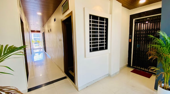 Un pasillo con suelo de baldosas, una ventana con diseño de cuadrícula y una puerta con reja de metal.