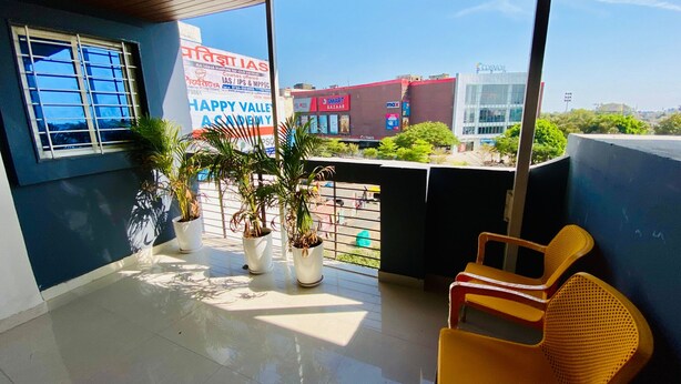 Een balkon met plantenbakken, een stoel en uitzicht op een winkelgebied.