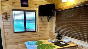 Un interior de madera con una mesa, un banco, una ventana, persianas y un televisor montado.